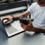 a man works on a laptop and phone